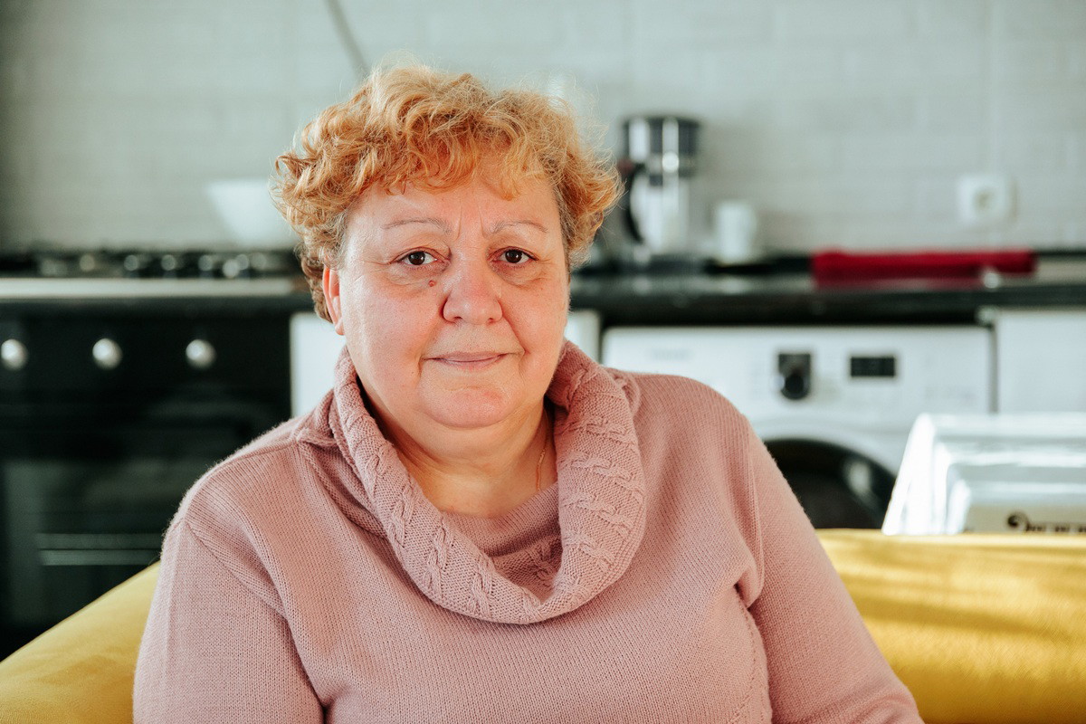 kobieta w wieku 60 plus w różowym swetrze siedzi w kuchni zamyślona