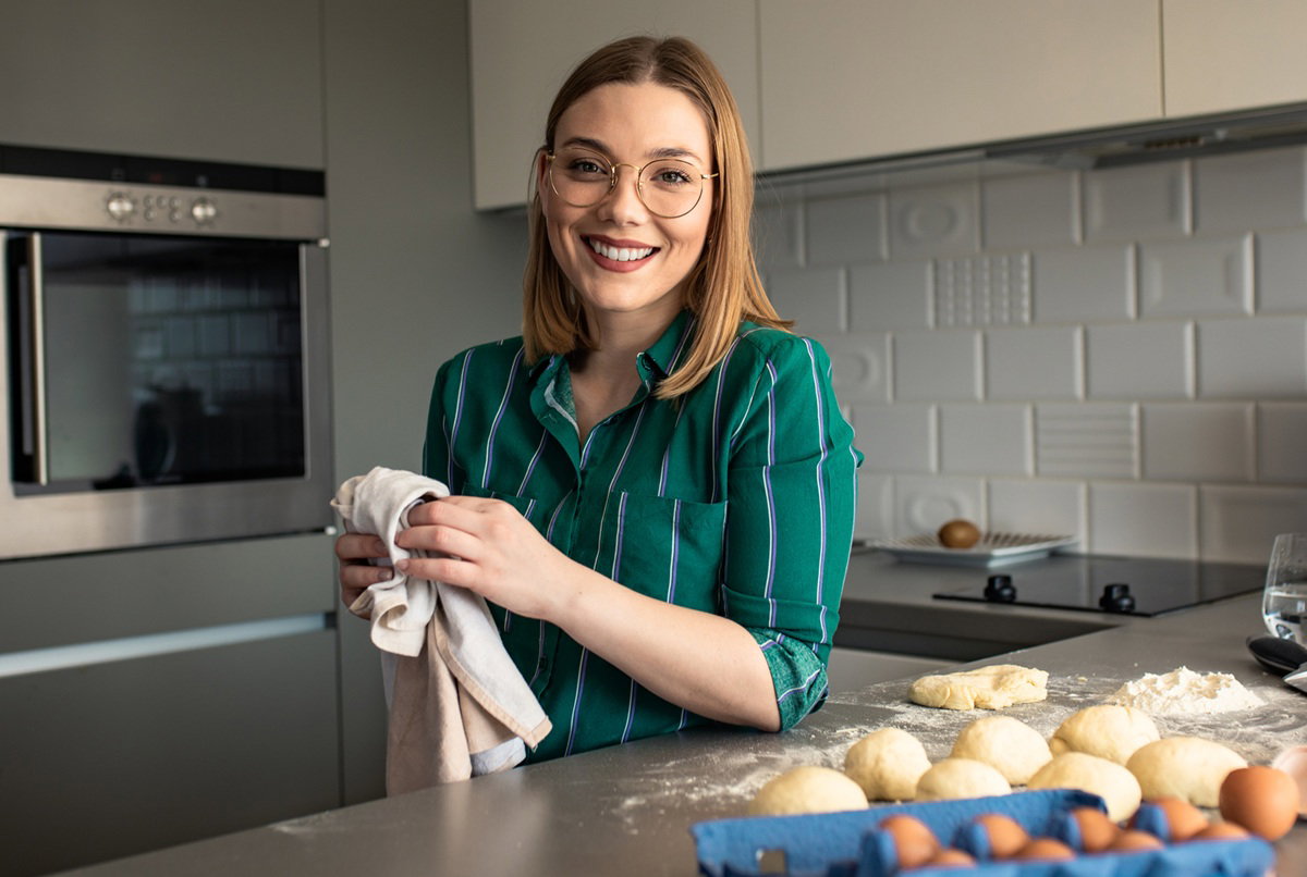 kobieta w wieku 30 plus w okularach stoi w kuchni robi pączki i uśmiecha się szeroko