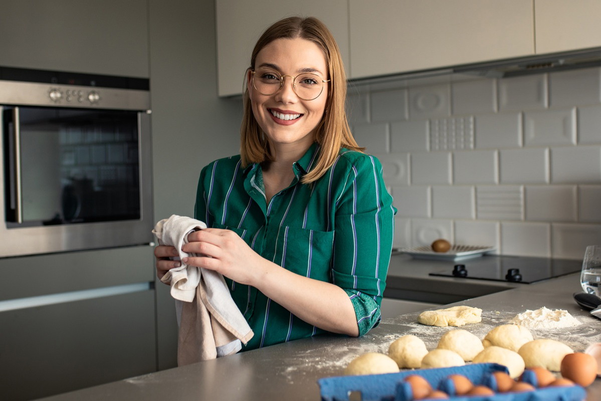 kobieta w wieku 30 plus w okularach stoi w kuchni robi pączki i uśmiecha się szeroko