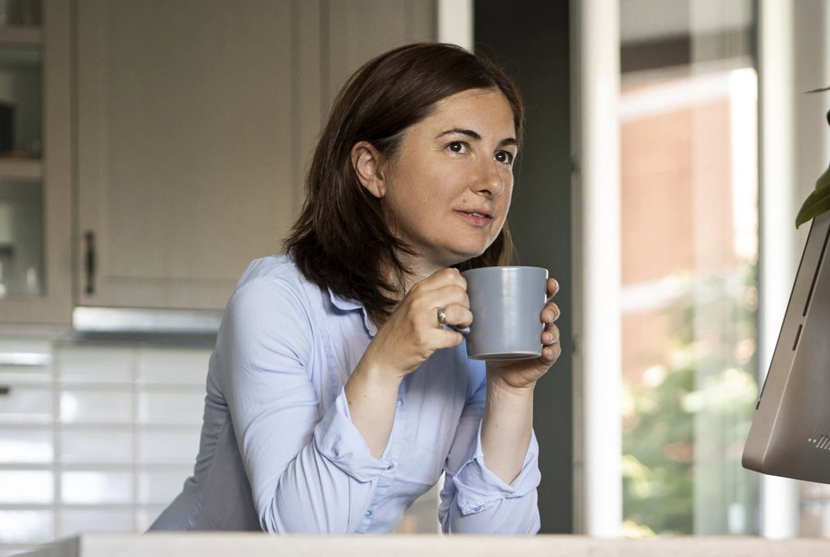 kobieta w wieku 30 plus stoi w kuchni z kubkiem herbaty zamyślona