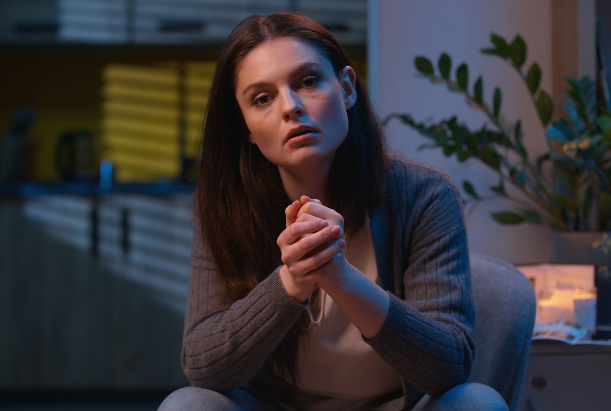 kobieta w wieku 35 plus siedzi załamana i smutna w ciemnym salonie