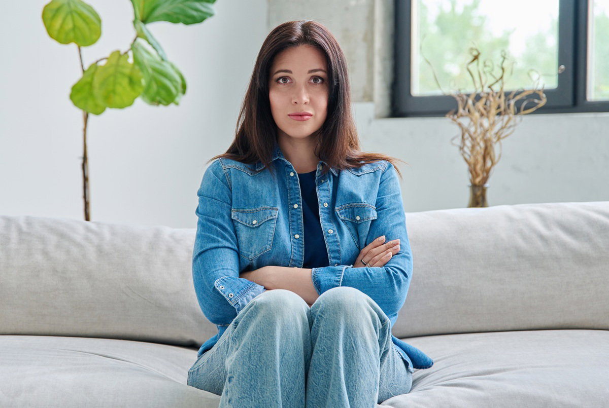 kobieta w wieku 30 plus w jeansowej koszuli siedzi na kanapie zdenerwowana