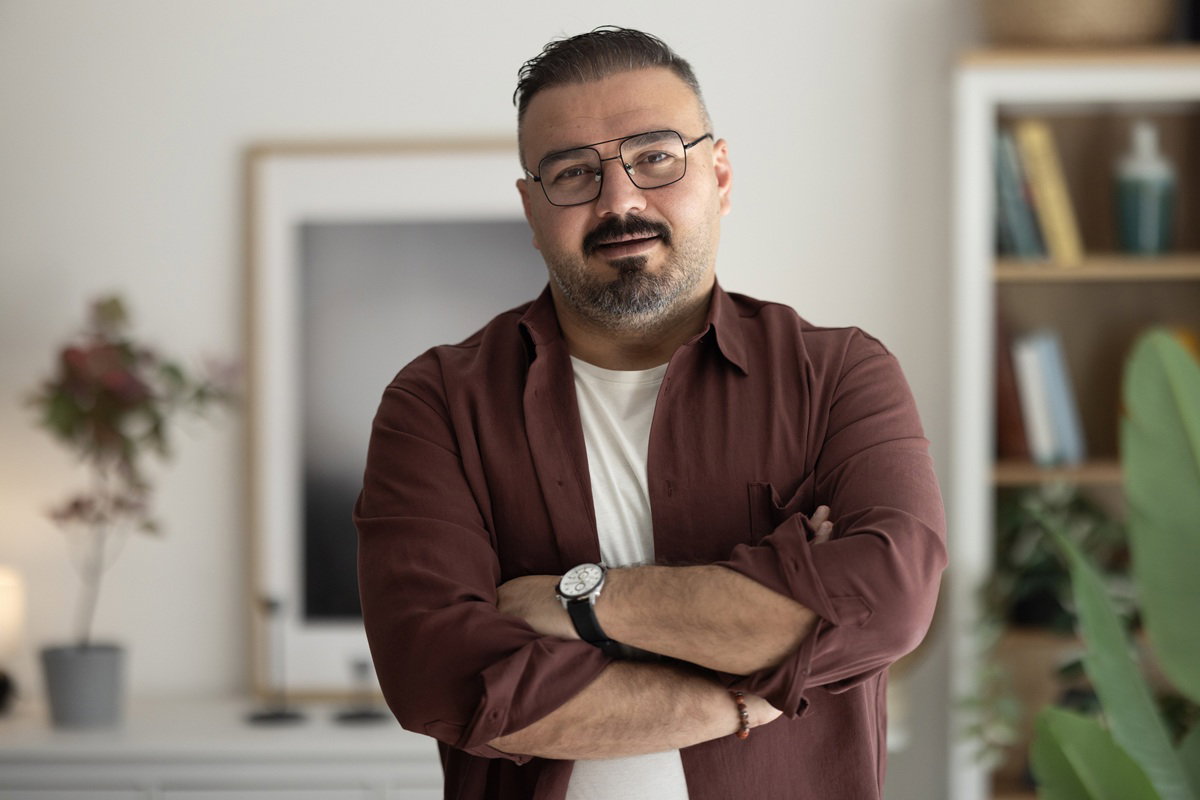 mężczyzna w wieku 30 plus w okularach stoi w pokoju i lekko się uśmiecha