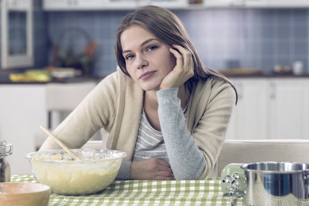 kobieta w wieku 30 plus siedzi w kuchni przy stole nad miską ciasta zamyślona i smutna
