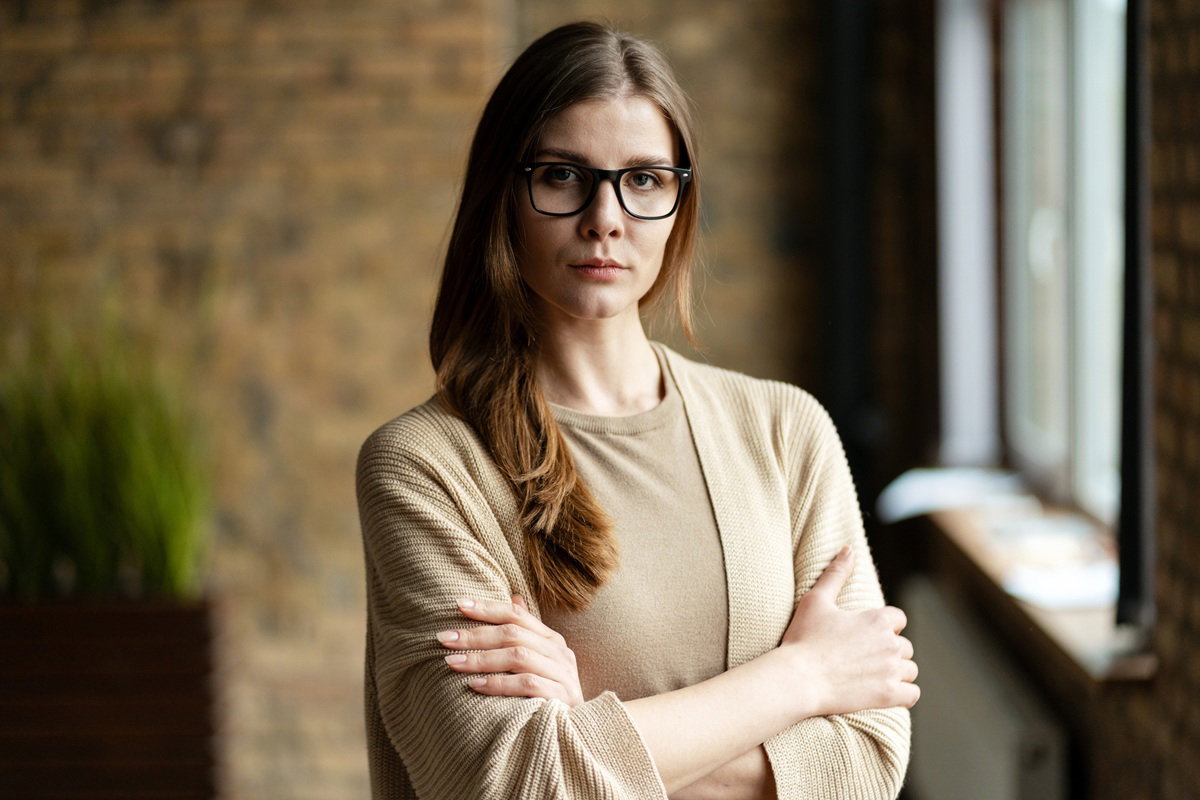 kobieta w wieku 35 plus w okularach w beżowym ubraniu stoi z poważną miną
