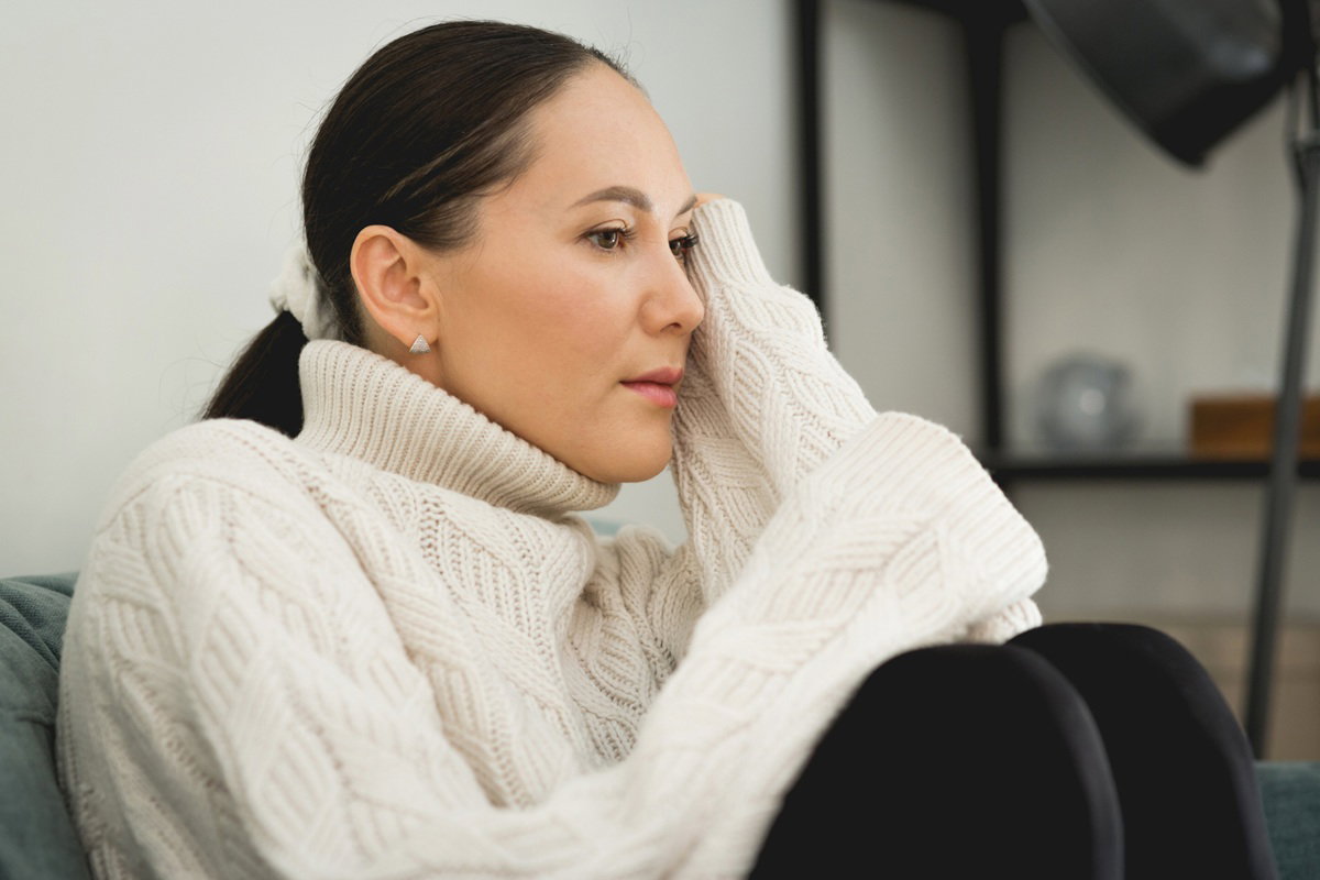 kobieta w wieku 35 plus z ciemnymi włosami w białym swetrze siedzi zamyślona