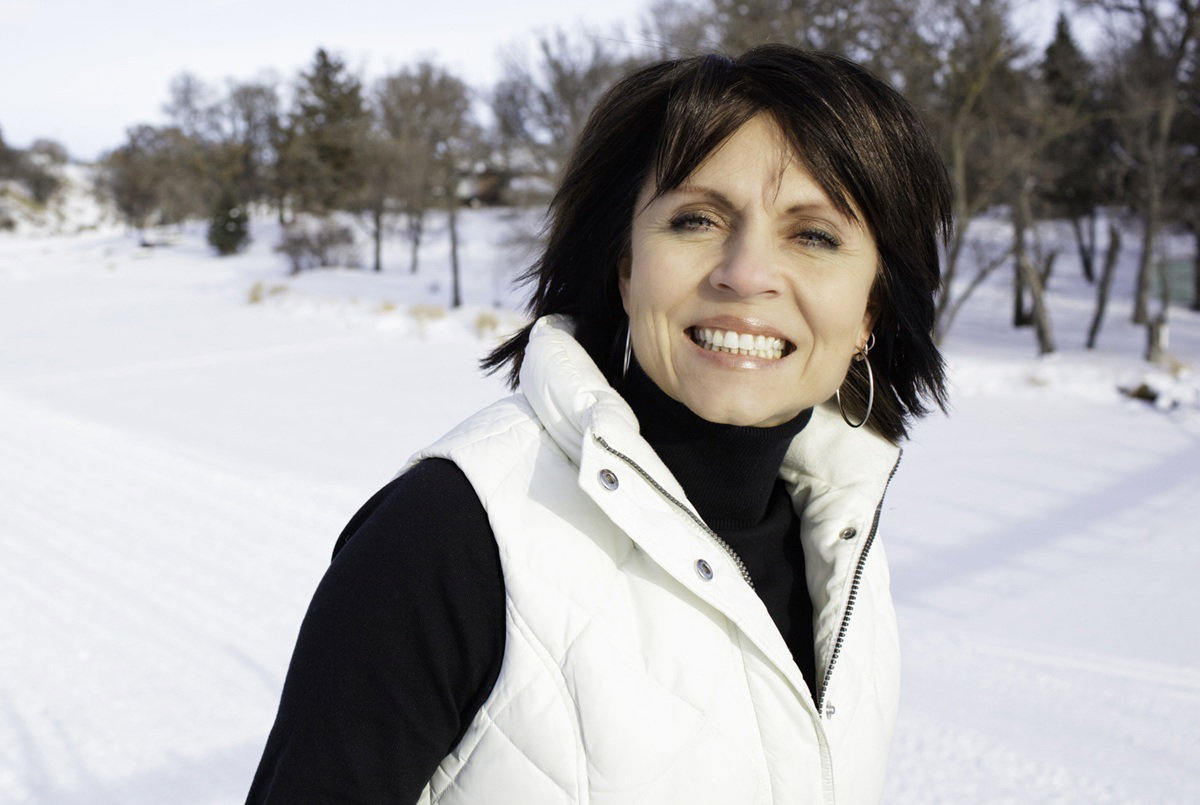 kobieta w wieku 45 plus z ciemnymi włosami stoi na tle zimowego pejzażu i się uśmiecha