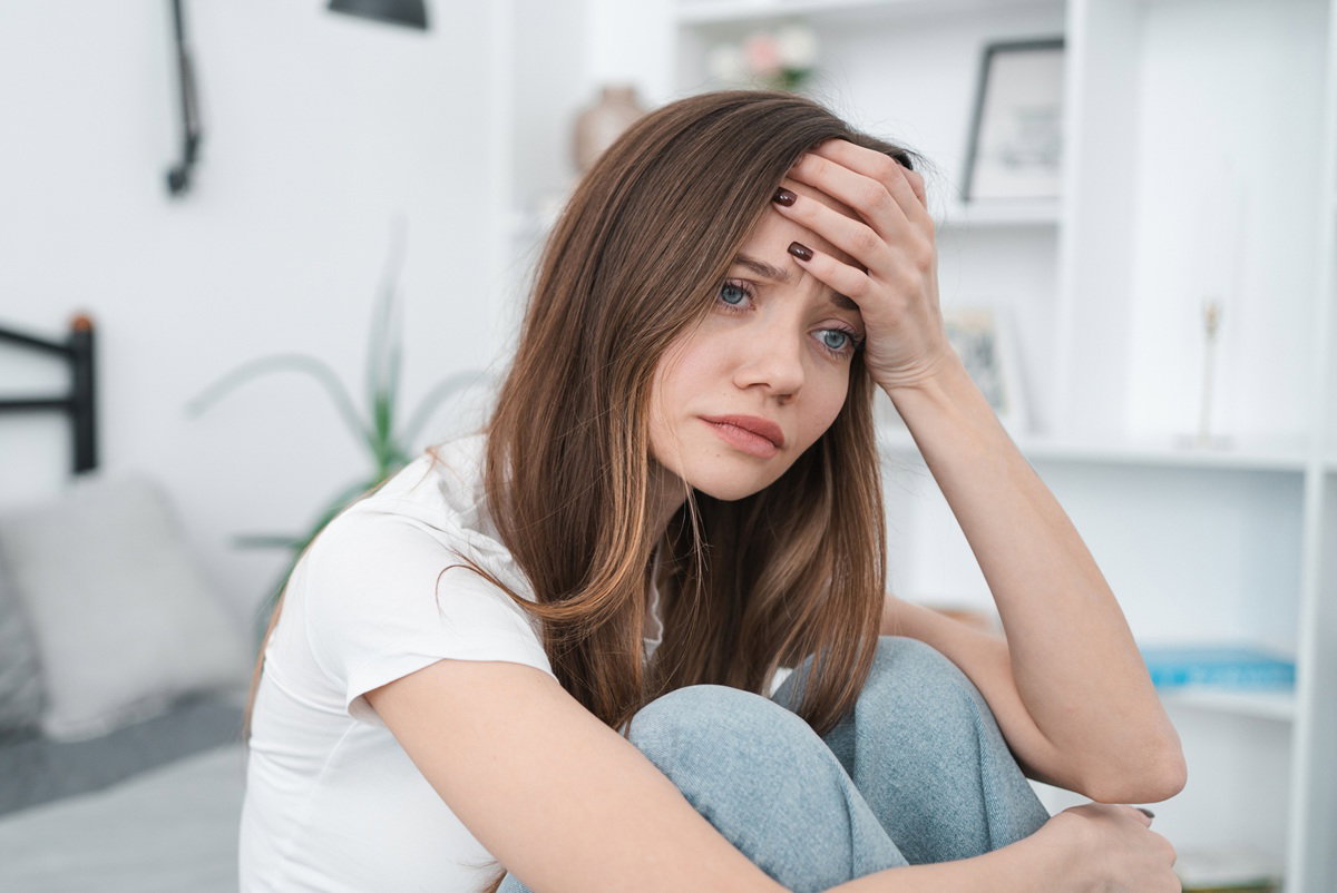 kobieta w wieku 30 plus z długimi włosami siedzi na kanapie w salonie załamana