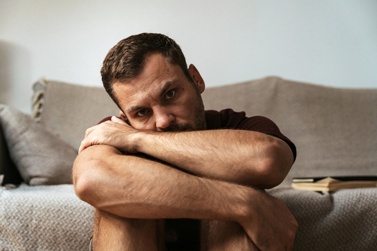 mężczyzna w wieku 30 plus załamany siedzi na podłodze koło kanapy