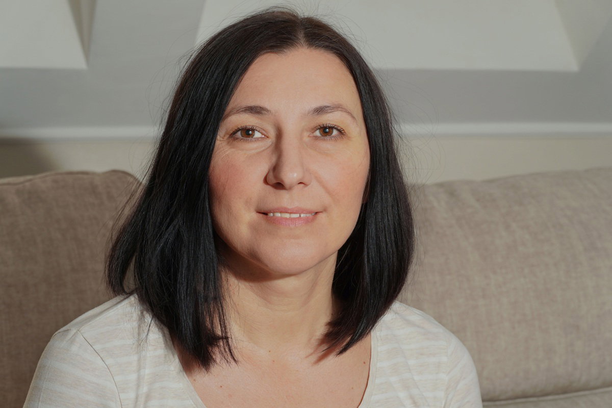 kobieta w wieku 40 plus z ciemnymi włosami siedzi na kanapie i uśmiecha się zadowolona