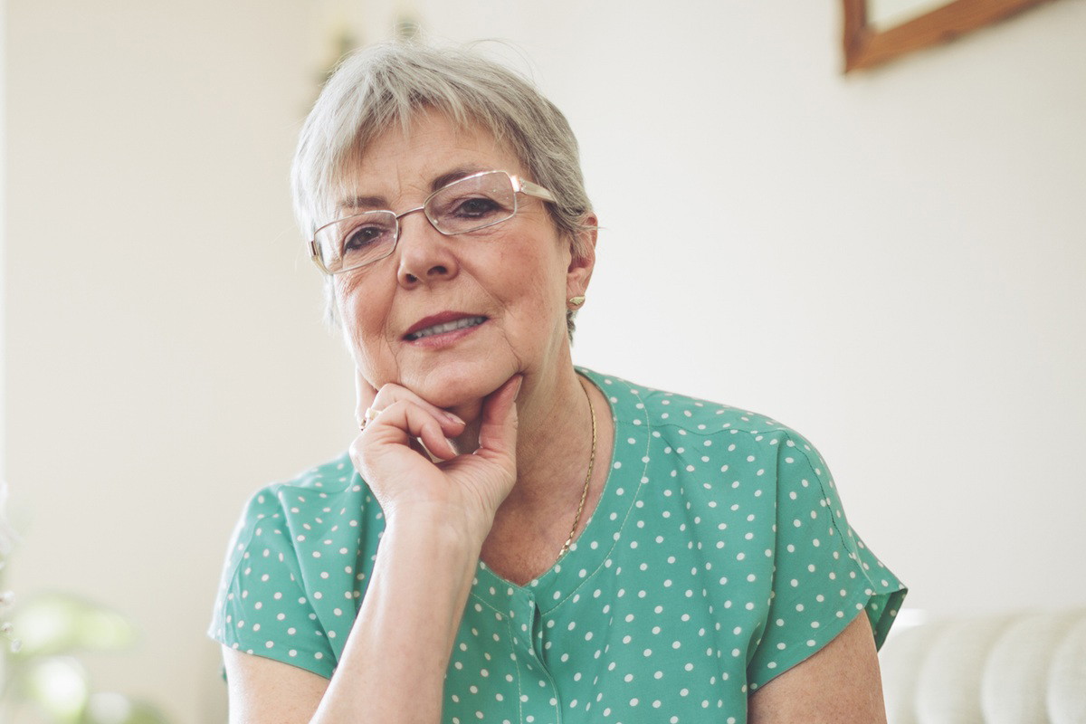 kobieta w wieku 60 plus w okularach z krótkimi włosami siedzi na kanapie zamyślona