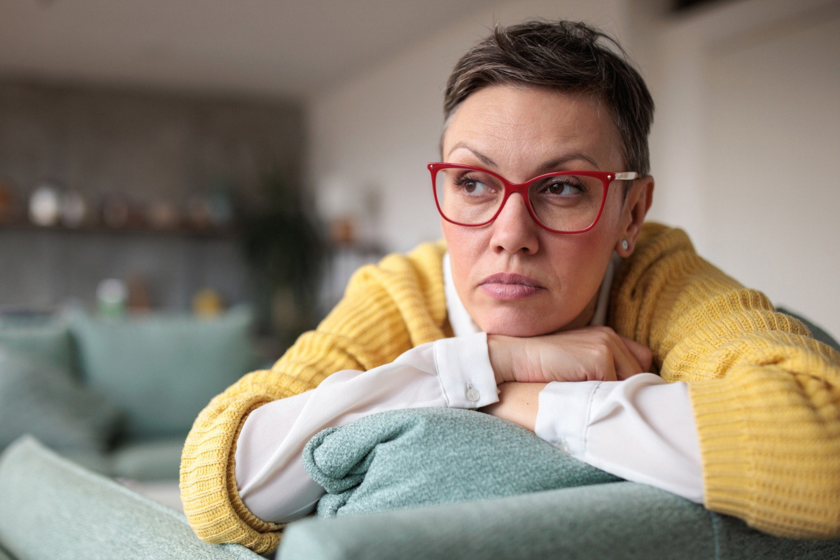 kobieta w wieku 45 plus w okularach i żółtym swetrze leży na kanapie zamyślona