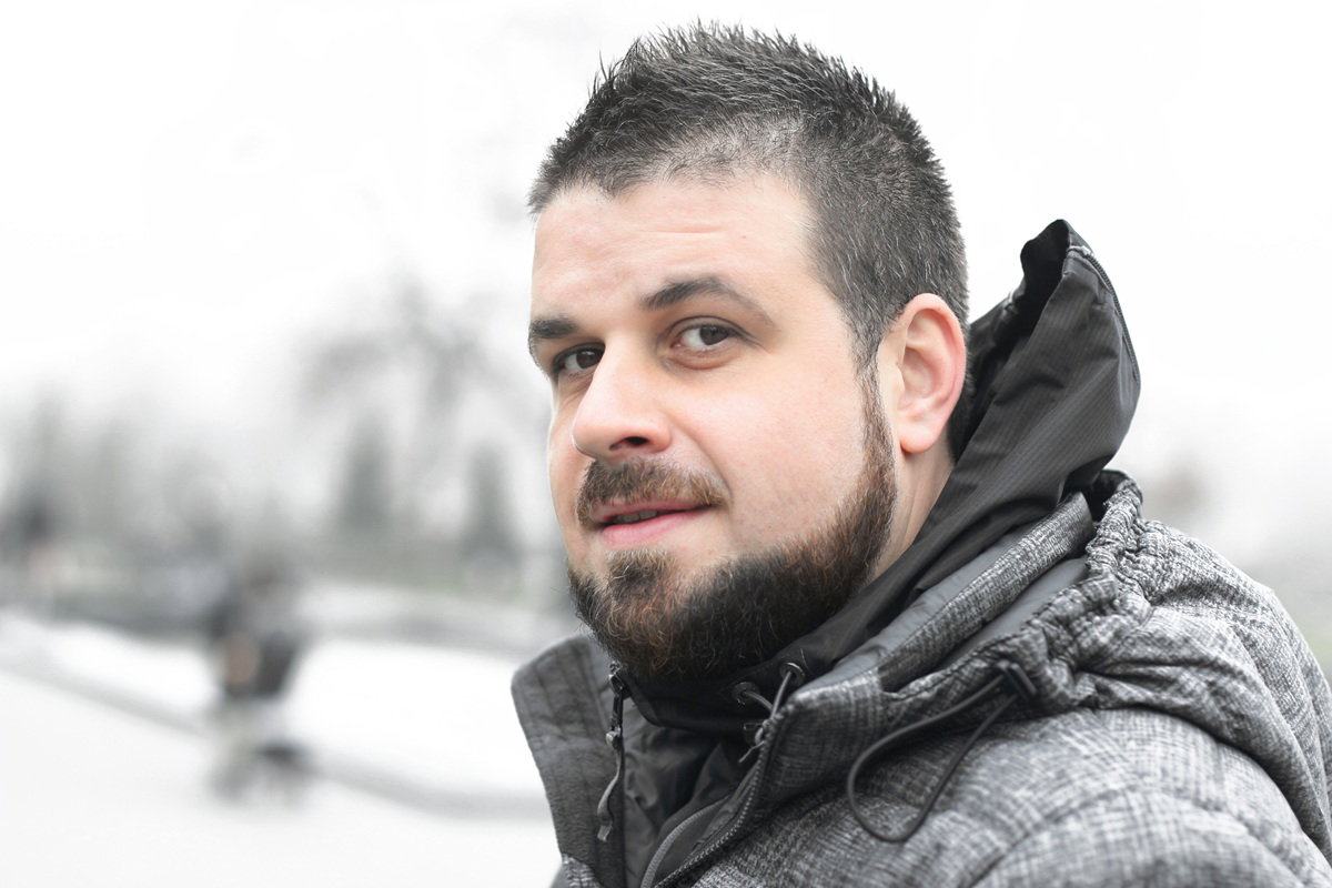 mężczyzna w wieku 30 plus z brodą i wąsami w kurtce stoi na zewnątrz zamyślony