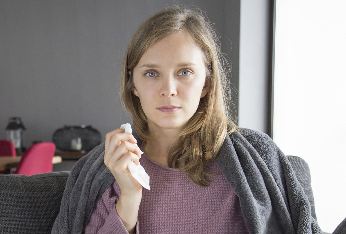 kobieta w wieku 30 plus z chusteczką w ręku zamyślona siedzi na kanapie