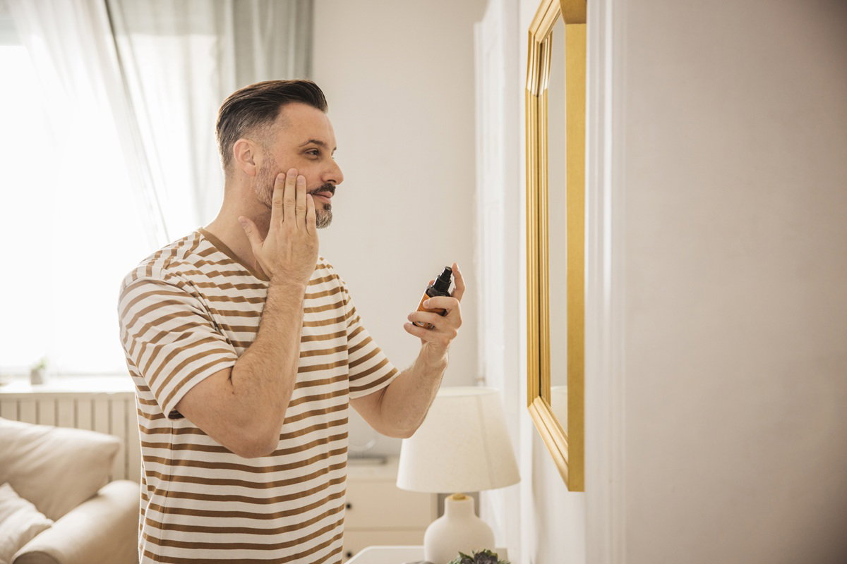 mężczyzna w wieku 40 plus stoi przed lustrem i wklepuje w twarz krem