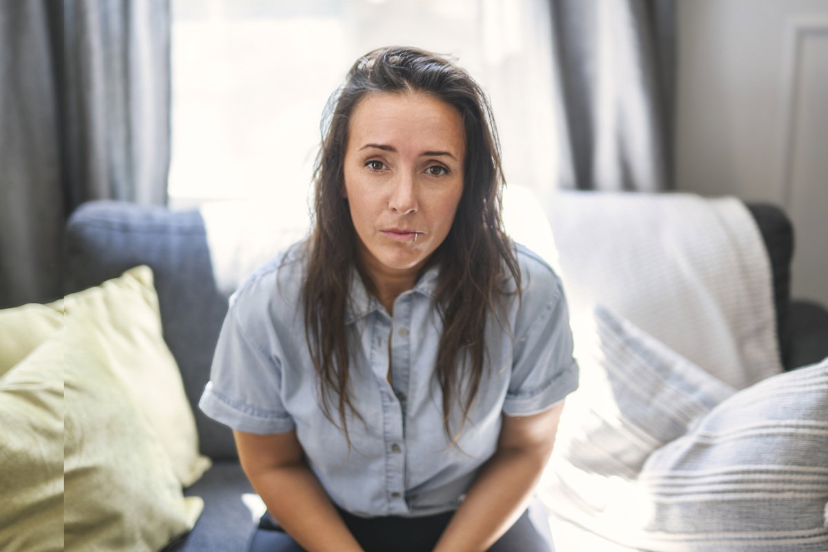 kobieta w wieku 30 plus w jasnej koszuli siedzi na kanapie smutna i zamyślona