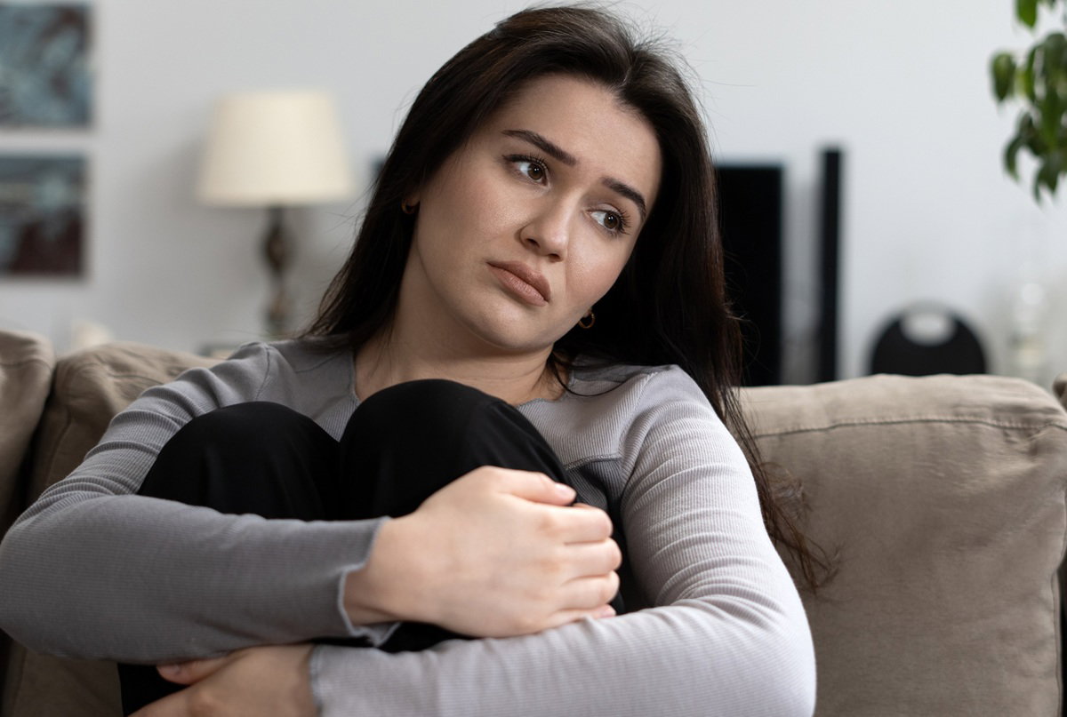 kobieta w wieku 30 plus z ciemnymi włosami siedzi na kanapie smutna i załamana