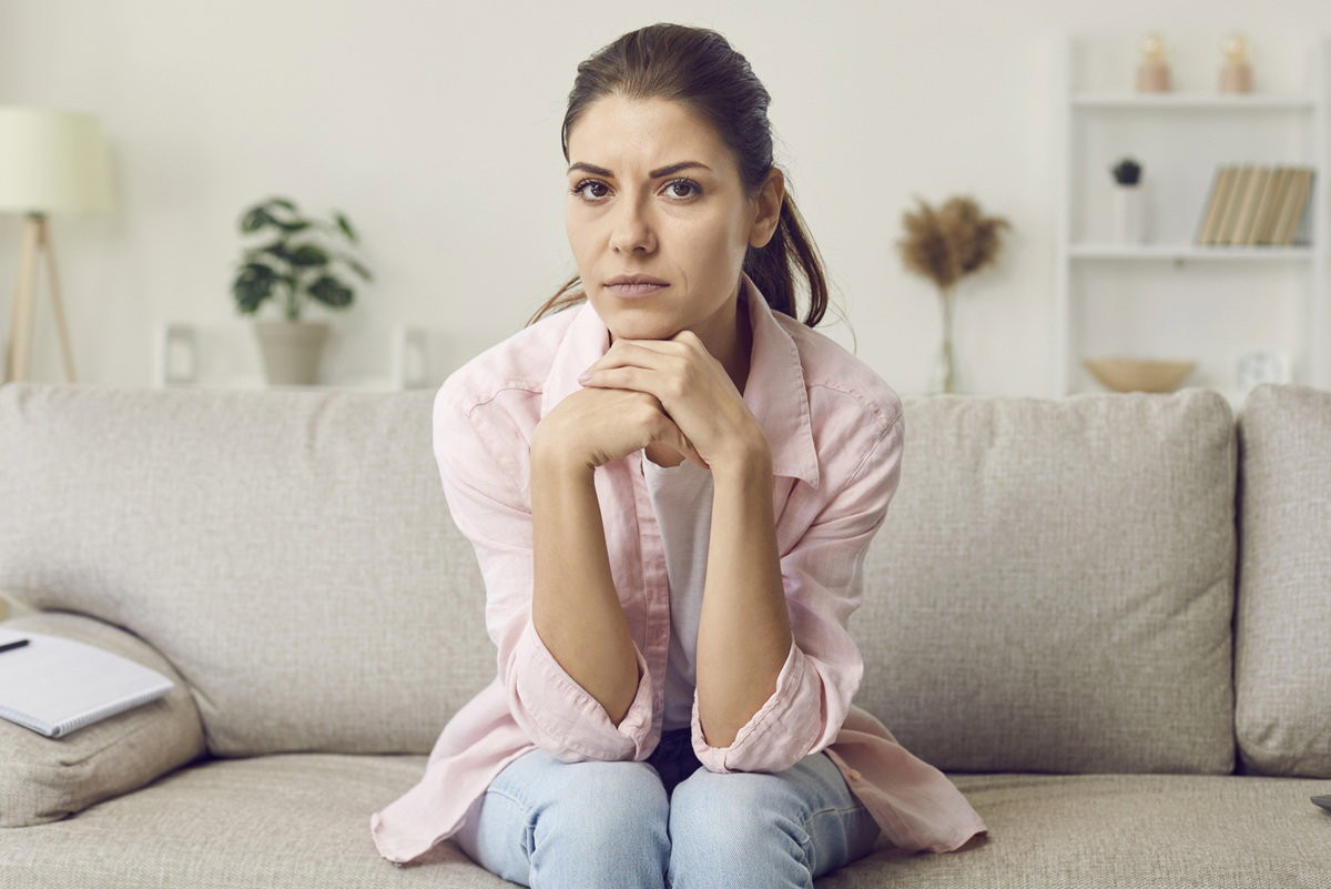 kobieta w wieku 25 plus w różowej koszuli na kanapie zmartwiona i zamyślona