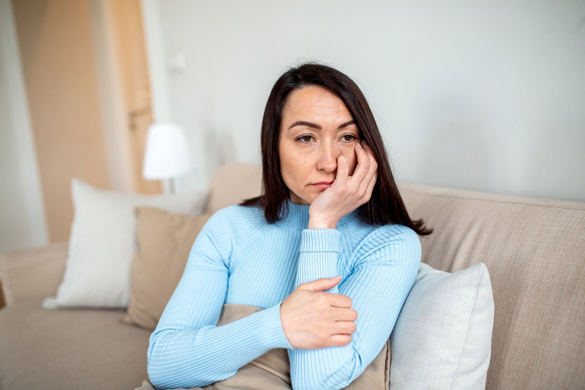 kobieta w wieku 35 plus z ciemnymi włosami siedzi na kanapie zamyślona