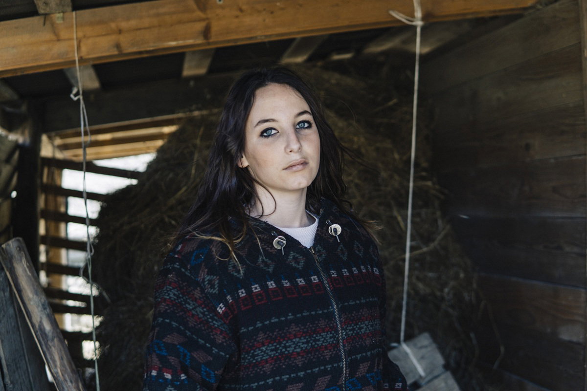 kobieta w wieku 25 plus z ciemnymi włosami stoi w stodole na tle siana smutna i zamyślona