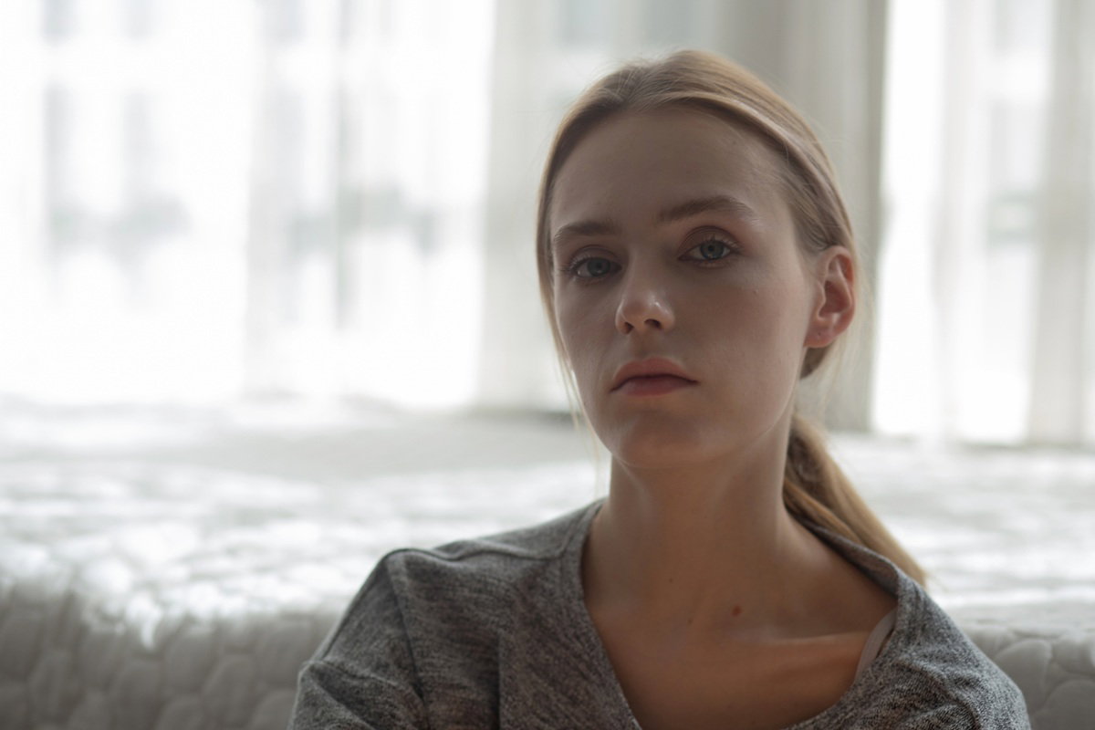 kobieta w wieku 25 plus blondynka siedzi na tle okna zamyślona i smutna