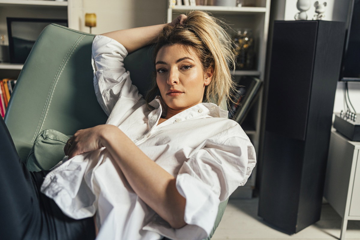 kobieta w wieku 30 plus blondynka siedzi na fotelu w rozluźnionej pozie i z poważnym wyrazem twarzy