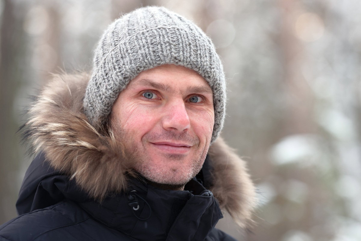 mężczyzna w wieku 40 plus w czarnej czapce i kurtce z kapturem stoi na tle zimowego lasu