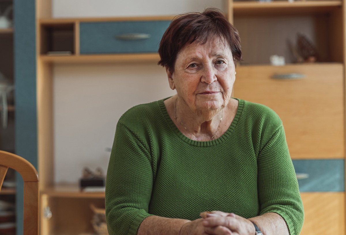 kobieta w wieku 65 plus w zielonym swetrze siedzi przy stole zmartwiona