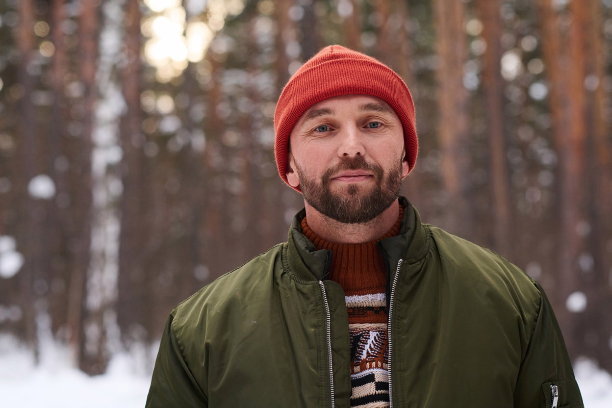 mężczyzna w wieku 40 plus z wąsami i broda w czerwonej czapace stoi na tle lasu
