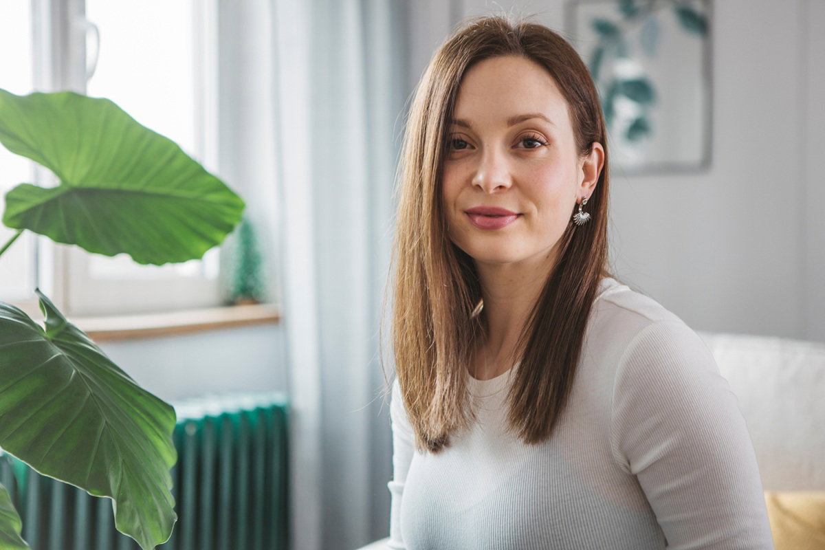 kobieta w wieku 30 plus z długimi włosami i ze srebrnymi kolczykami siedzi w domu i lekko się uśmiecha
