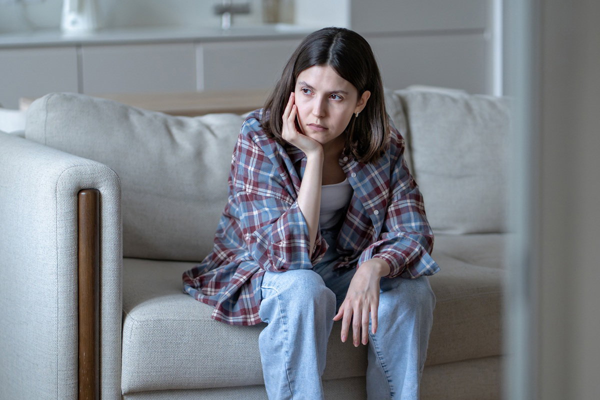 kobieta w wieku 30 plus w kraciastej koszuli siedzi zmartwiona na kanapie