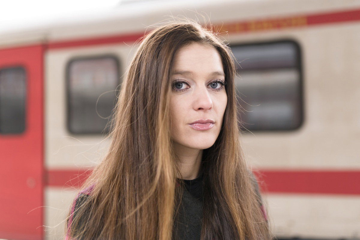kobieta w wieku 30 plus z długimi włosami stoi na tle wagonu z poważną miną