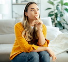 kobieta w wieku 35 plus w żółtej bluzce siedzi na kanapie zamyślona