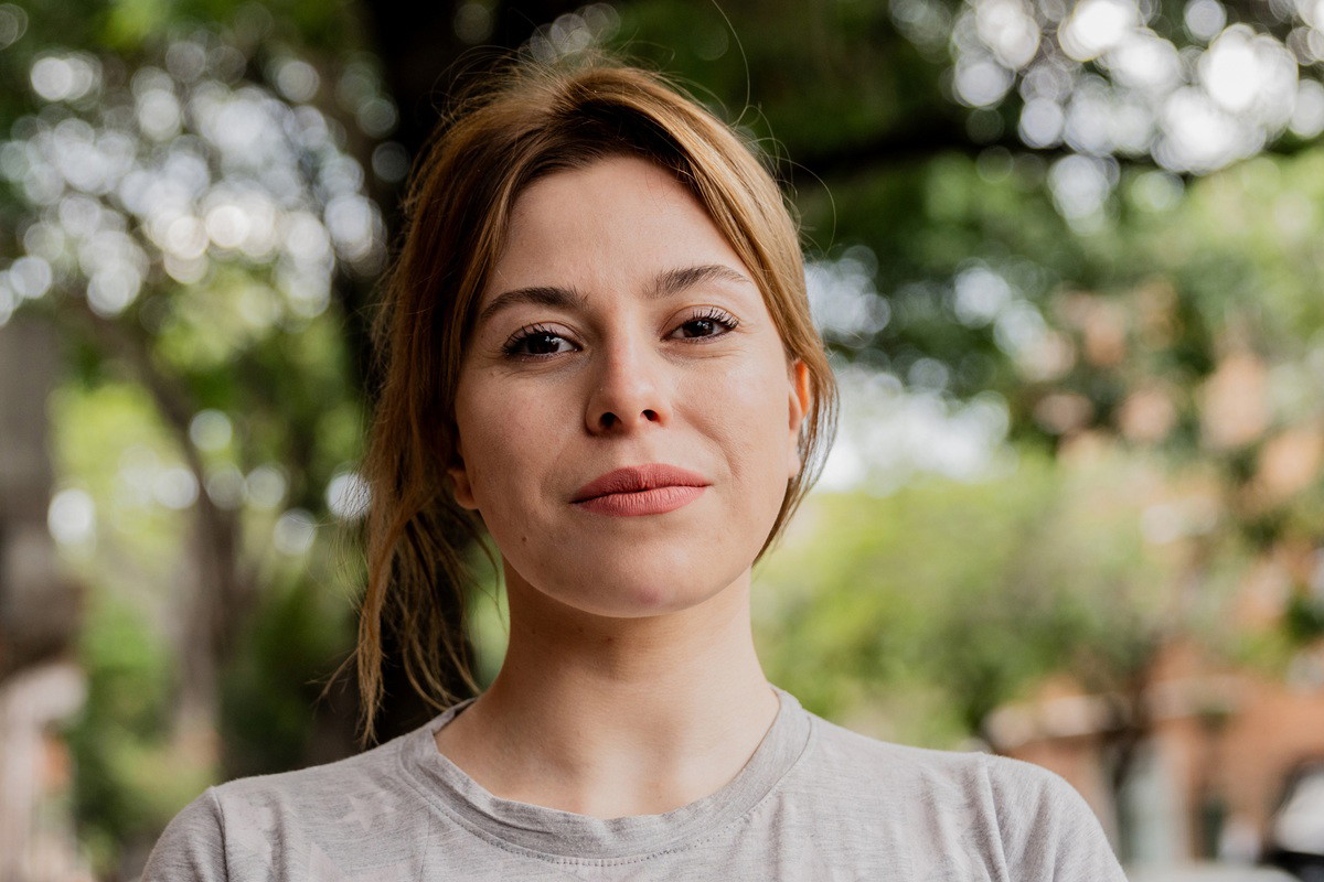 kobieta w wieku 30 plus w jasnym t-shircie stoi na zewnątrz na tle zielenie poważna