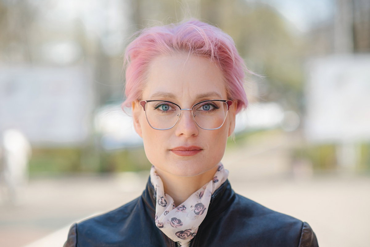 kobieta w wieku 35 plus z różowymi krótkimi włosami stoi na zewnątrz z poważną miną