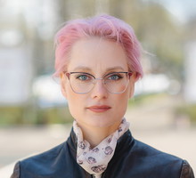 kobieta w wieku 35 plus z różowymi krótkimi włosami stoi na zewnątrz z poważną miną