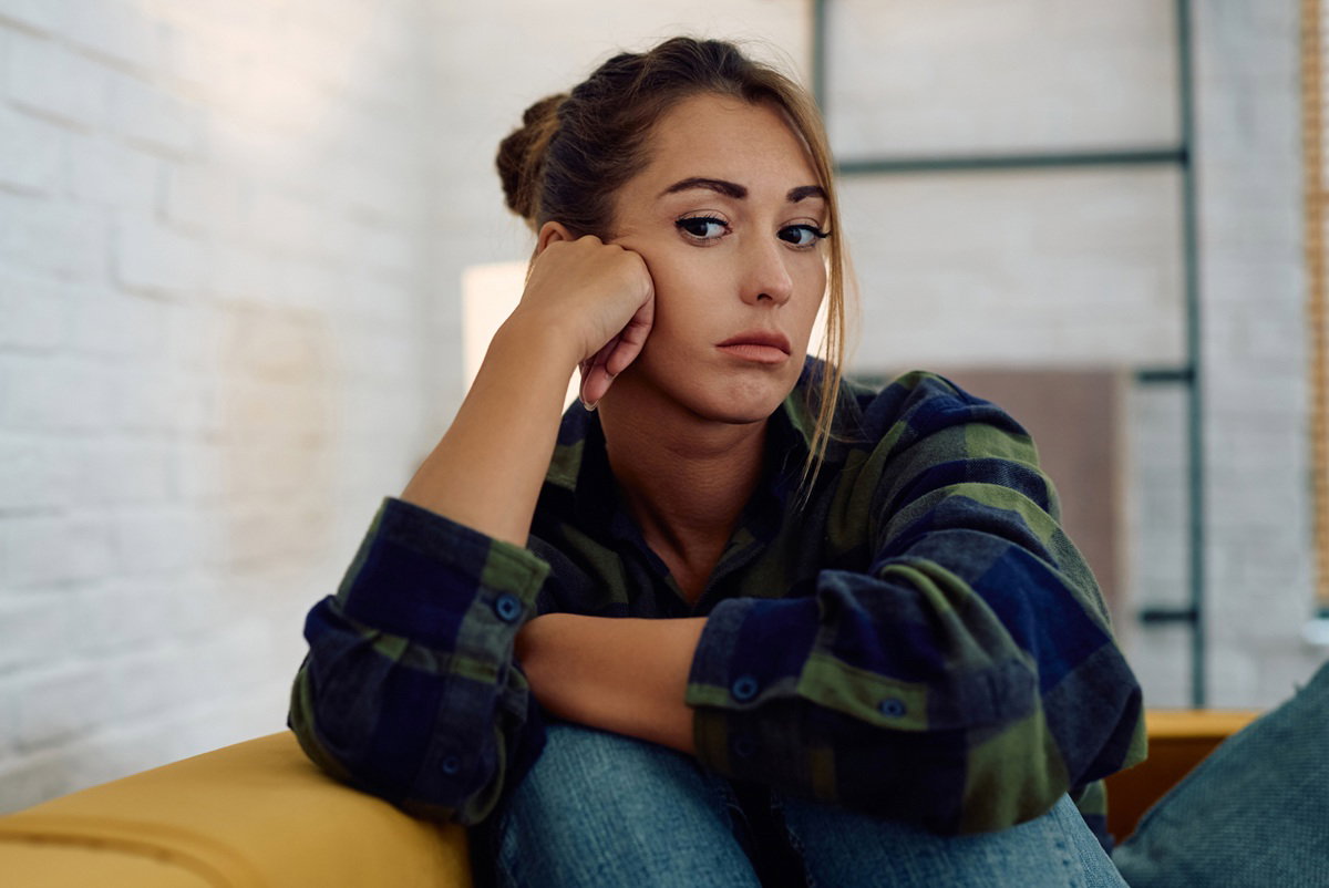 kobieta w wieku 25 plus w koszuli w kratę siedzi na żółtej kanapie załamana