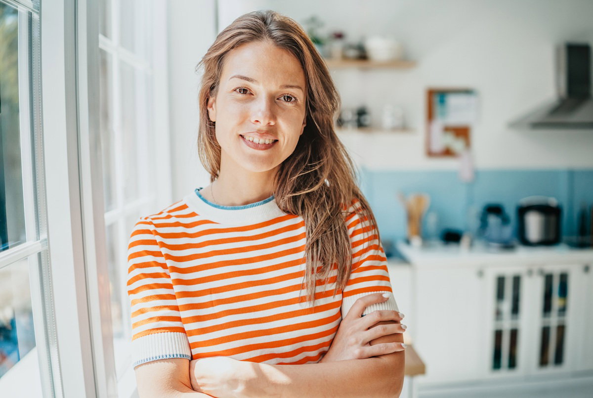kobieta w wieku 30 plus w pasiastej bluzce stoi na tle kuchni lekko uśmiechnięta