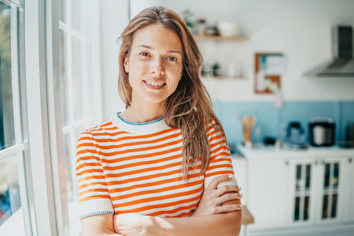 kobieta w wieku 30 plus w pasiastej bluzce stoi na tle kuchni lekko uśmiechnięta