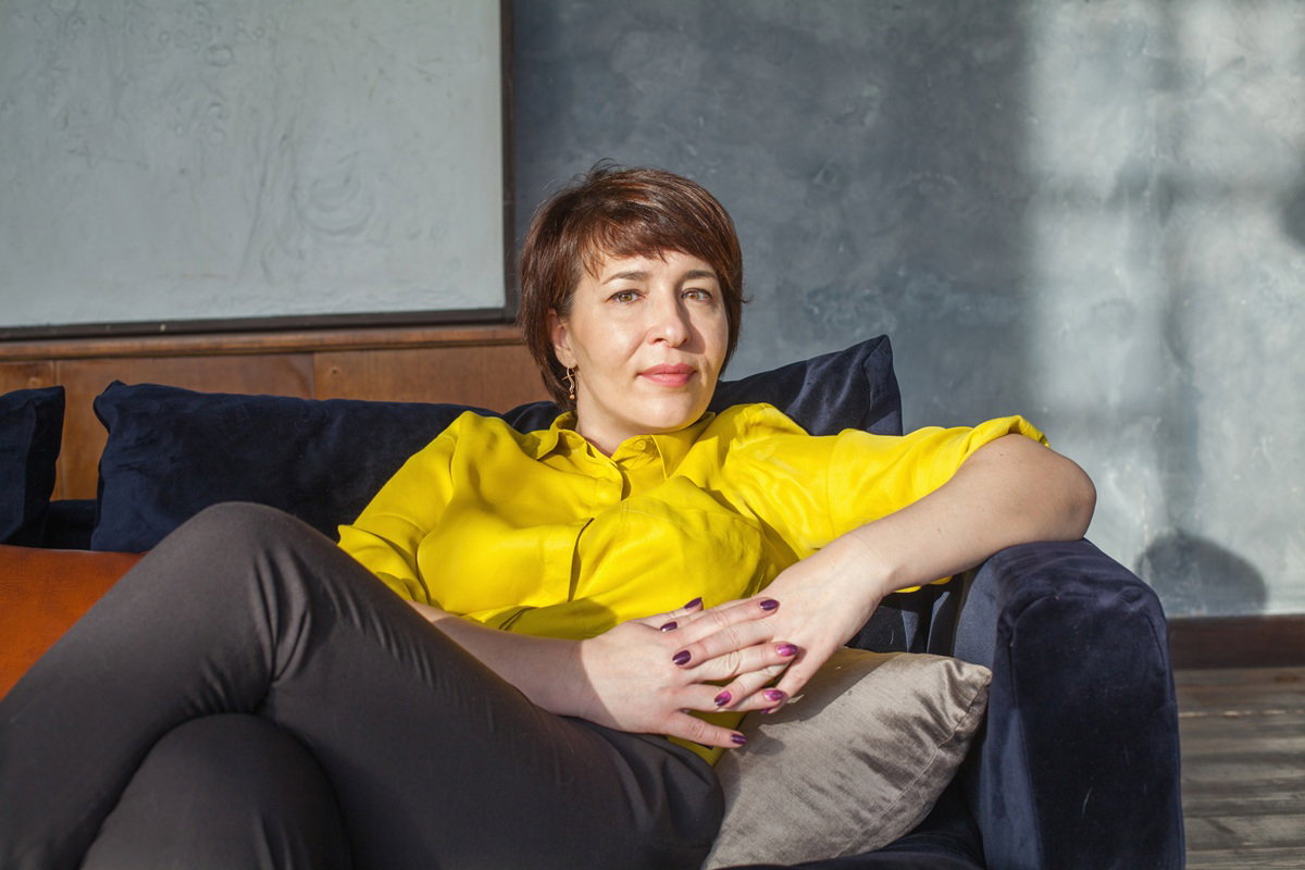 kobieta w wieku 40 plus w żółtej bluzce siedzi na kanapie z poważną miną