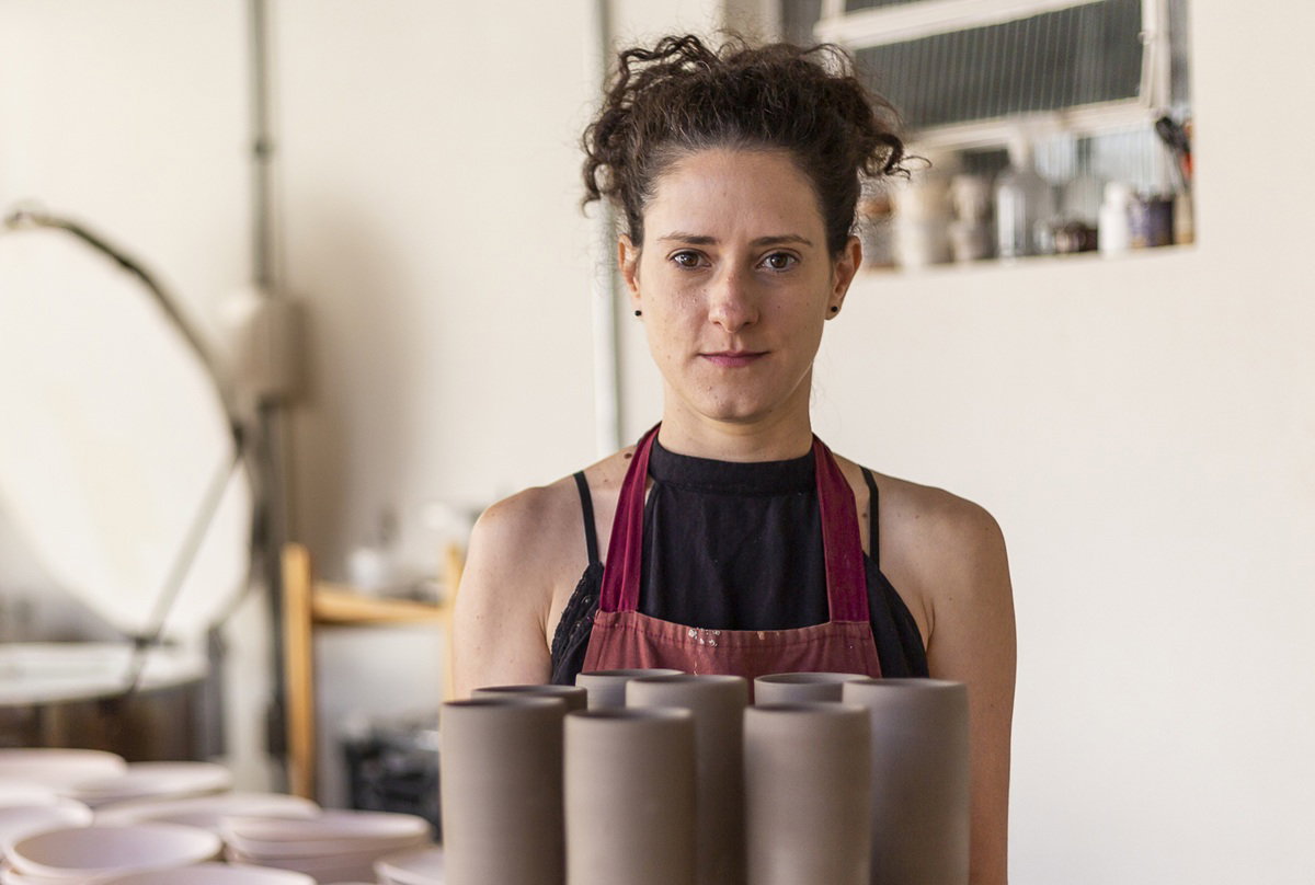 kobieta w wieku 35 plus stoi z poważną miną w pracowni ceramicznej z autorskimi naczyniami