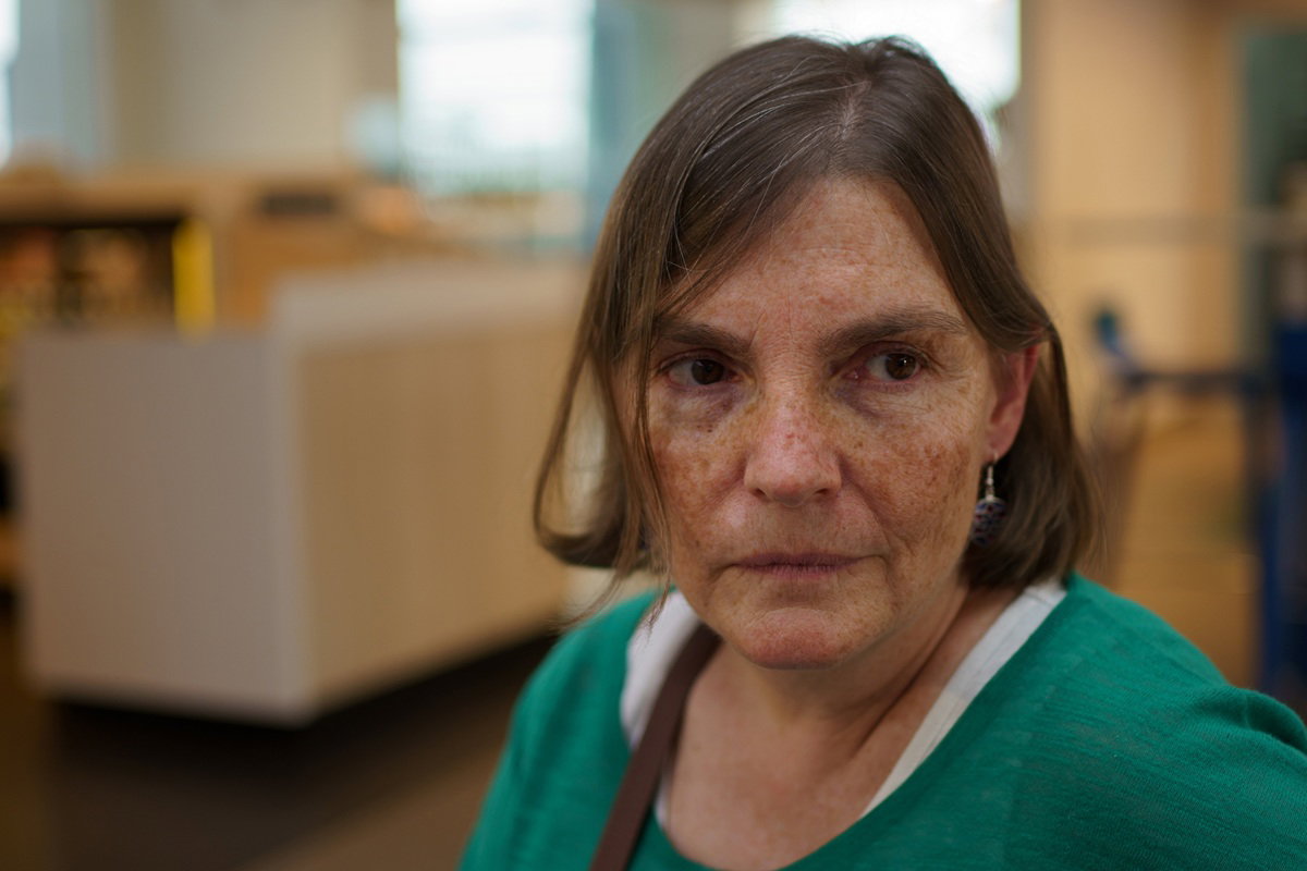 kobieta w wieku 55 plus z piegami w zielonej bluzce stoi w salonie załamana i smutna