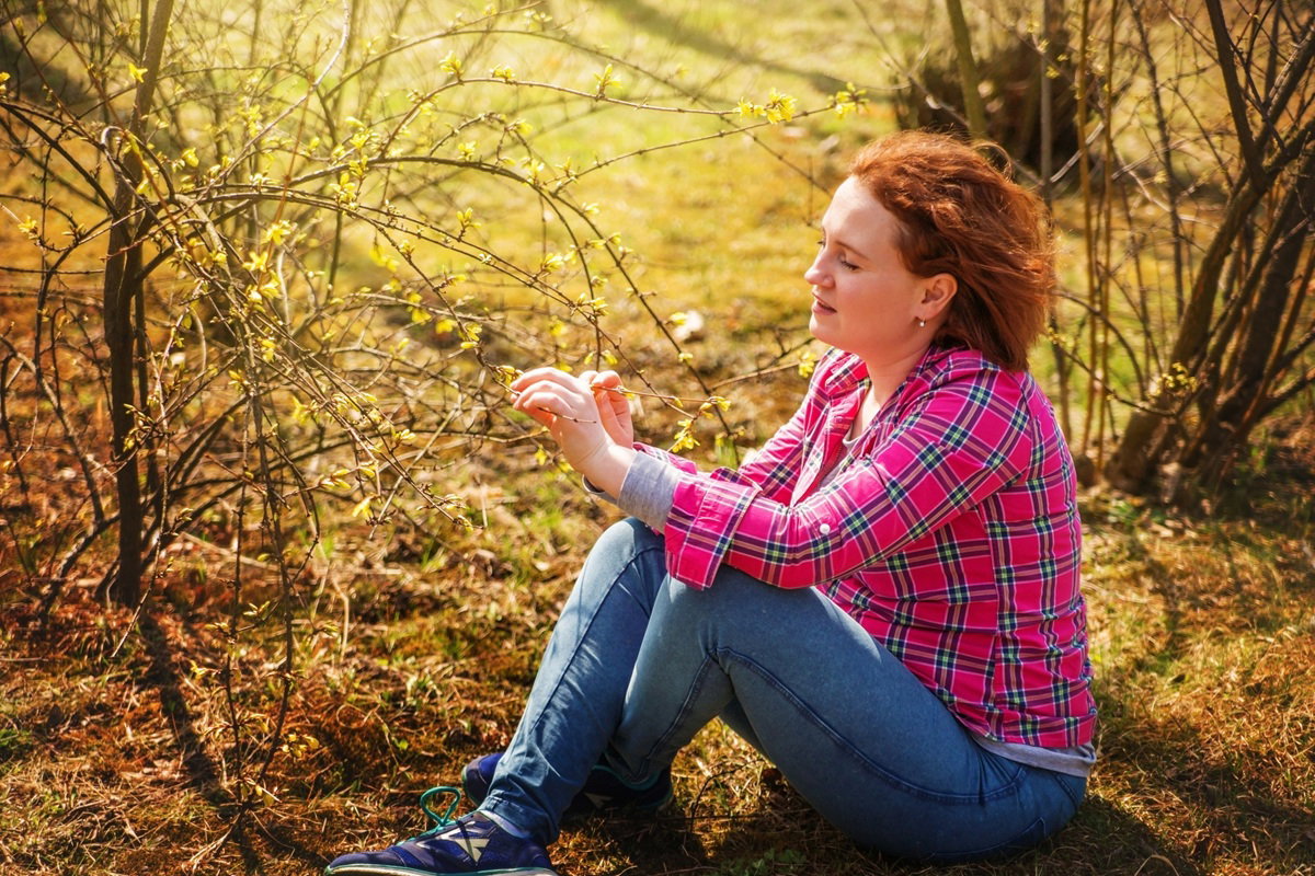 kobieta w wieku 30 plus w kraciastej koszuli siedzi na ziemi przy krzaczku forsycji