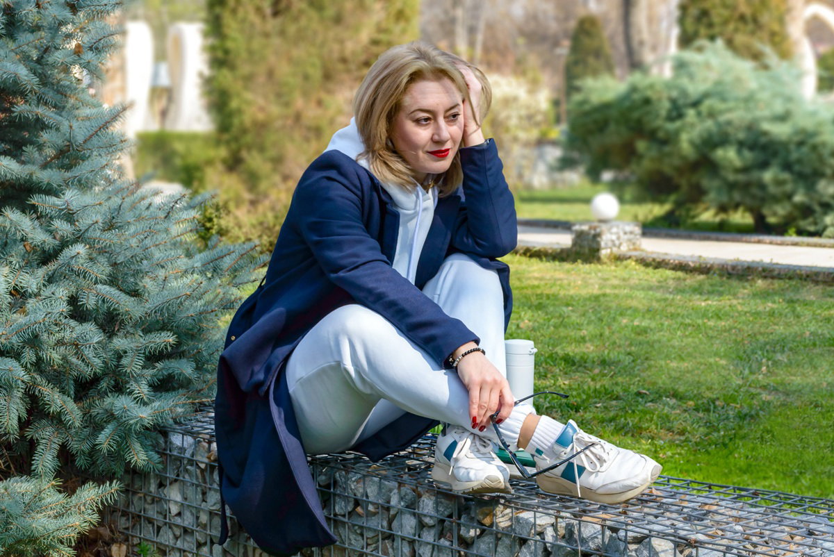 kobieta w wieku 40 plus siedzi w płaszczu w ogrodzie zamyślona