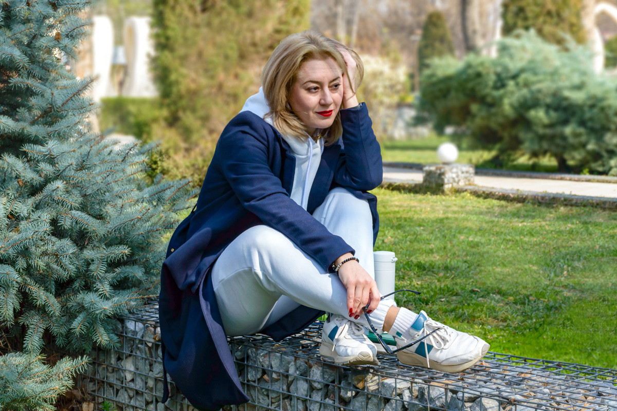 kobieta w wieku 40 plus siedzi w płaszczu w ogrodzie zamyślona