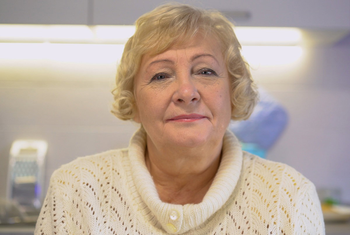 kobieta w wieku 60 plus w białym swetrze blondynka siedzi w kuchni z pobłażliwą miną