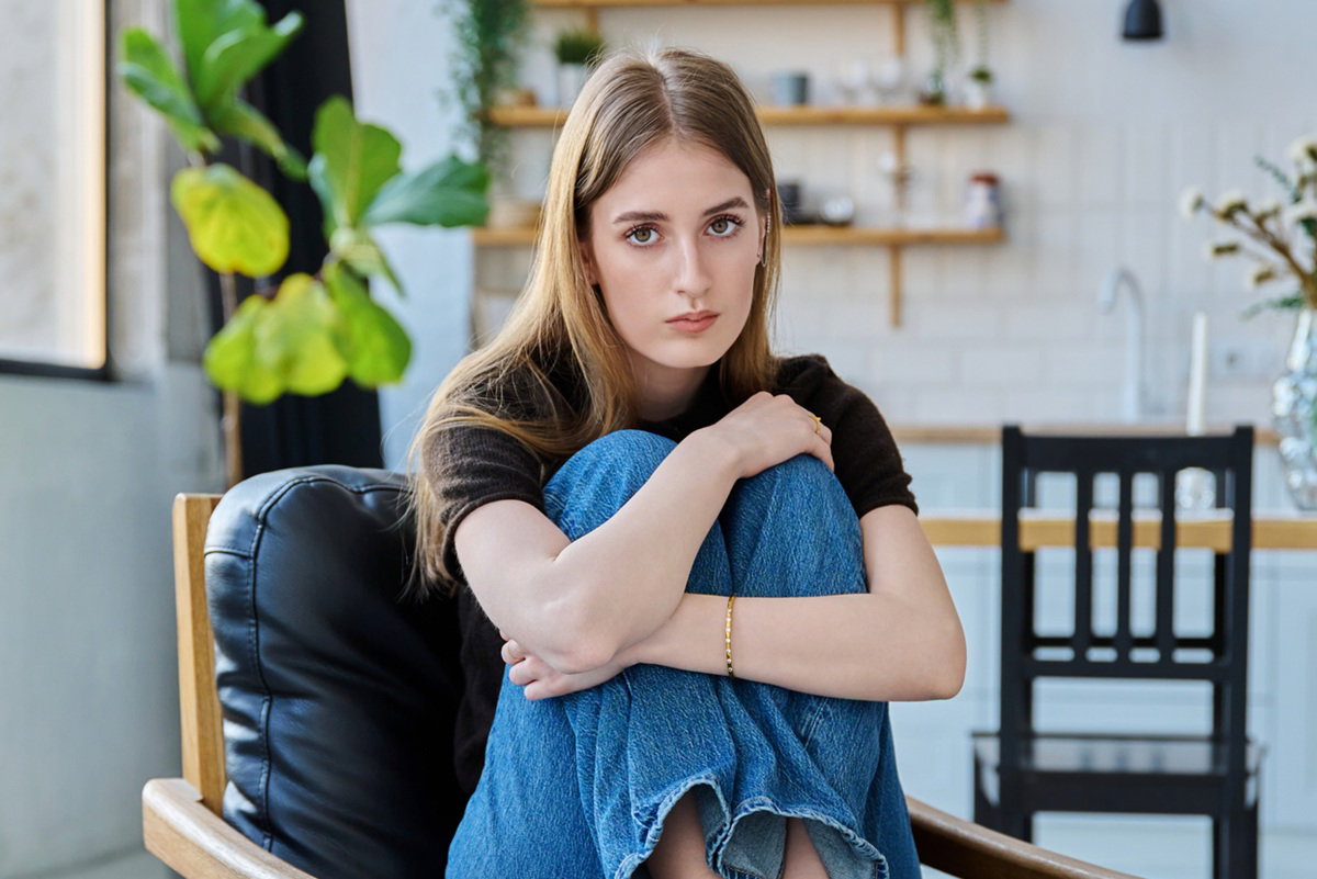 młoda kobieta w wieku 15 plus siedzi na fotelu na tle kuchni smutna
