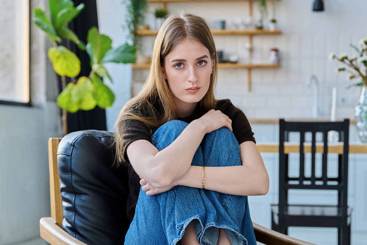 młoda kobieta w wieku 15 plus siedzi na fotelu na tle kuchni smutna