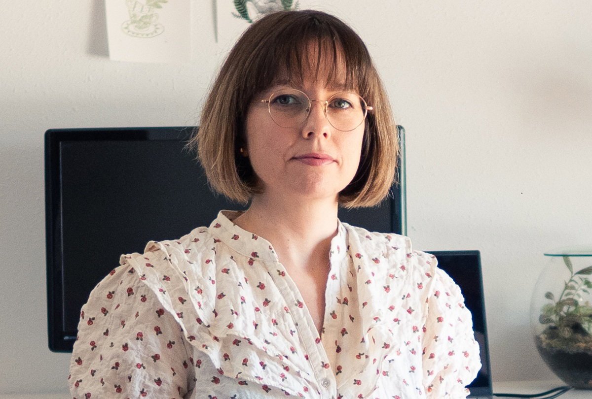 kobieta w wieku około 40 lat w okularach siedzi na tle ekranu komputera z poważną miną