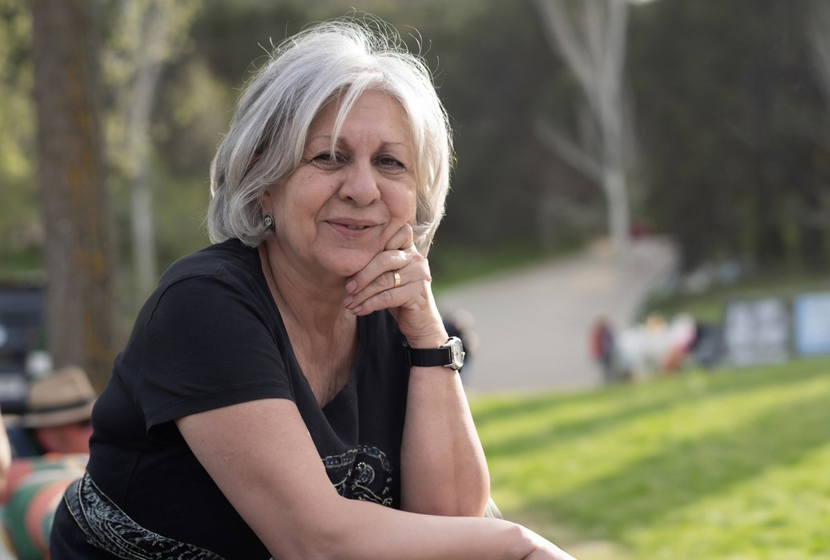 kobieta w wieku 65 lat siwe włosy stoi na ganku na tle wiosennego ogrodu zamyślona